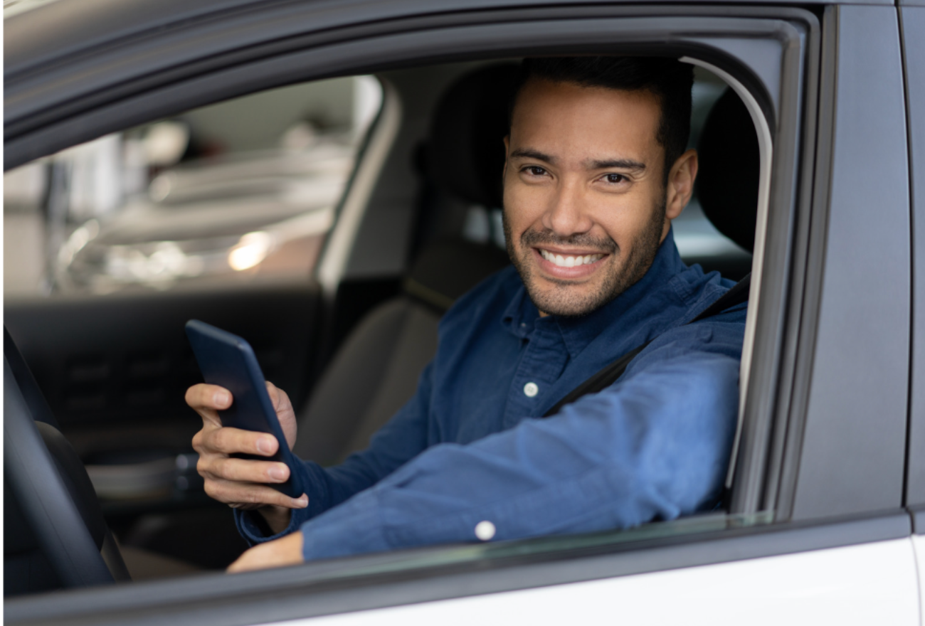 Homem feliz utilizando um aplicativo do Primeira Placa no carro, demonstrando a facilidade de emplacar um veículo 0 km de forma rápida e simples.