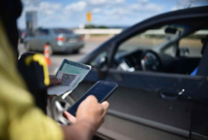 Motorista mostrando documentação do veículo, em frente ao carro estacionado.