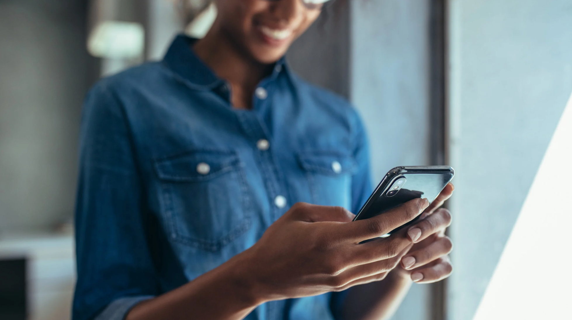 Mulher sorridente usando o celular para acessar um aplicativo, representando a praticidade de resolver documentação veicular com o Primeira Placa.