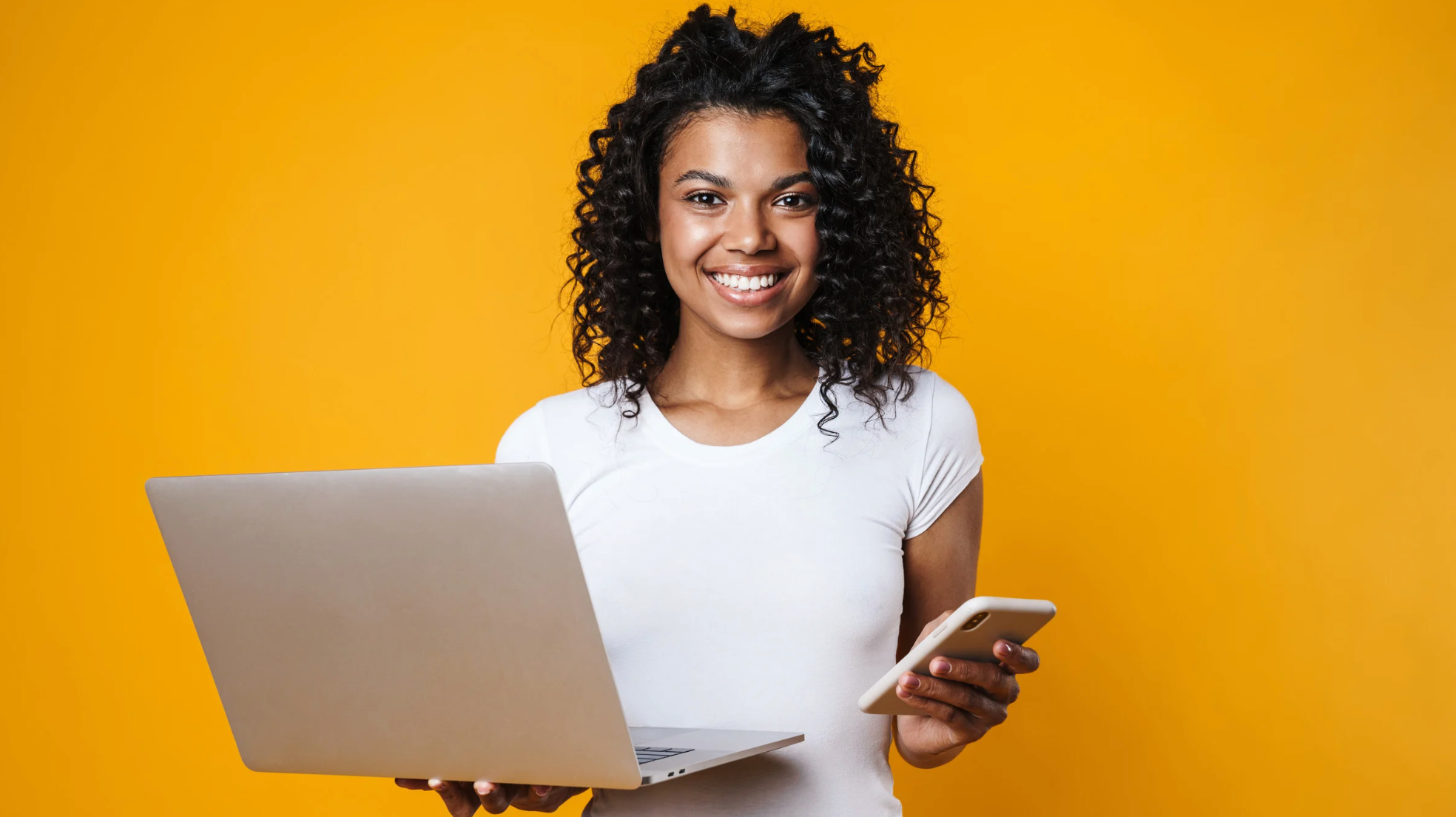 Mulher sorrindo, segurando um notebook e um celular, representando praticidade na resolução de pendências pelo aplicativo.