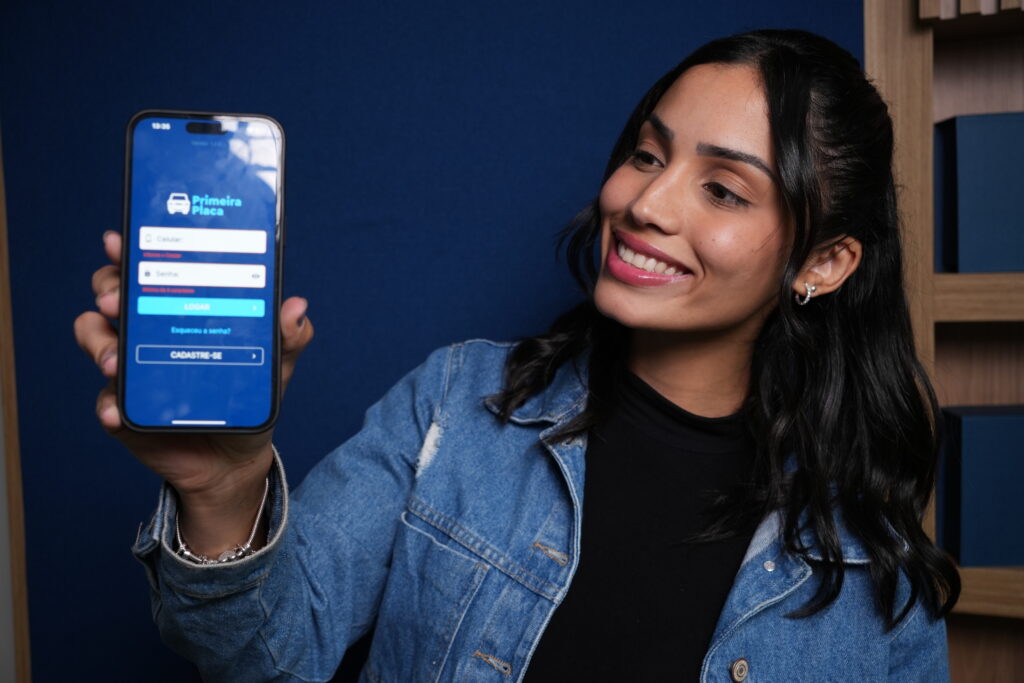 Jovem segurando um smartphone com a tela do aplicativo Primeira Placa aberta, representando praticidade e confiança no emplacamento de veículo online barato.