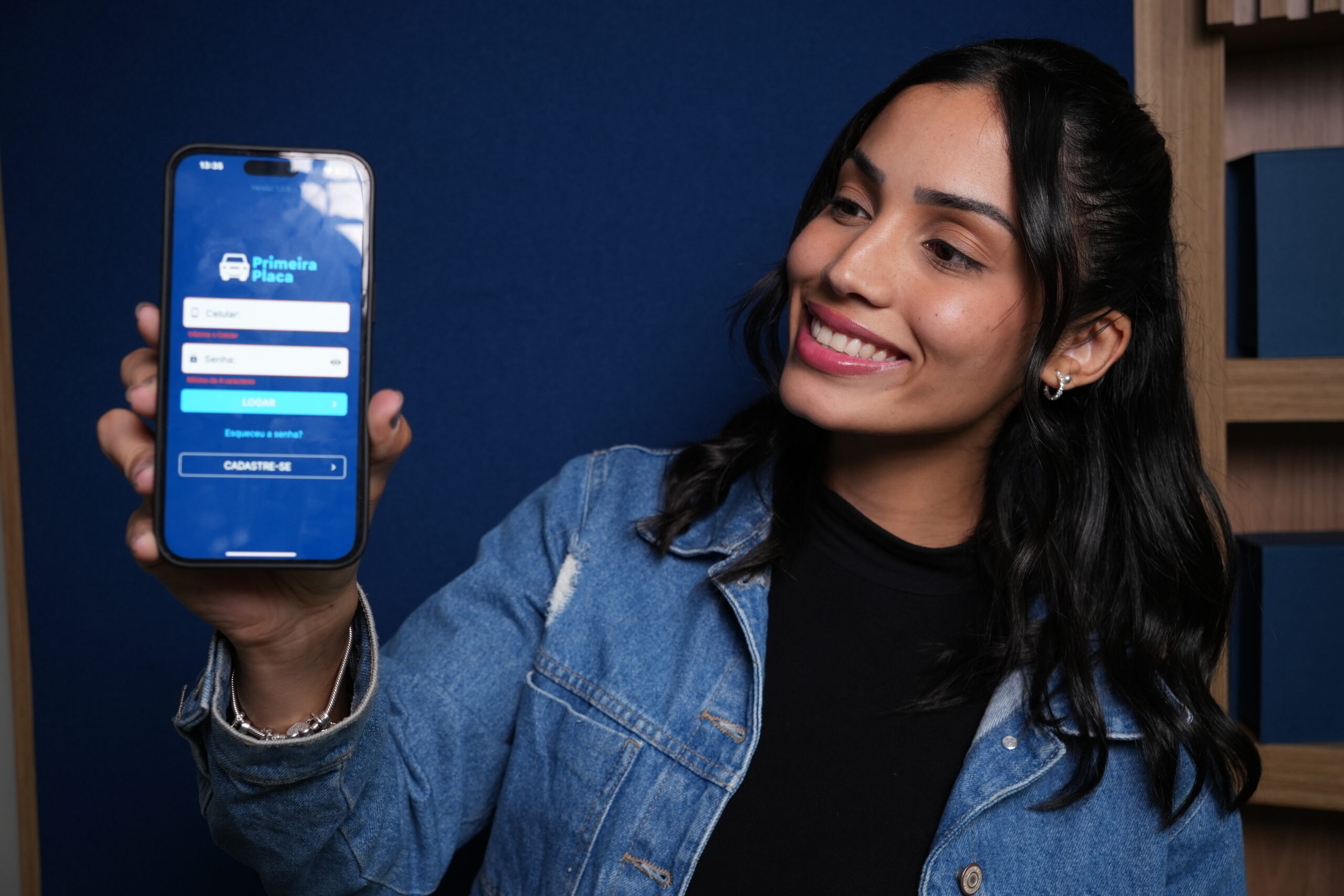 Jovem  sorridente mostra o app Primeira Placa no celular, simbolizando praticidade no emplacamento de carro 0km.