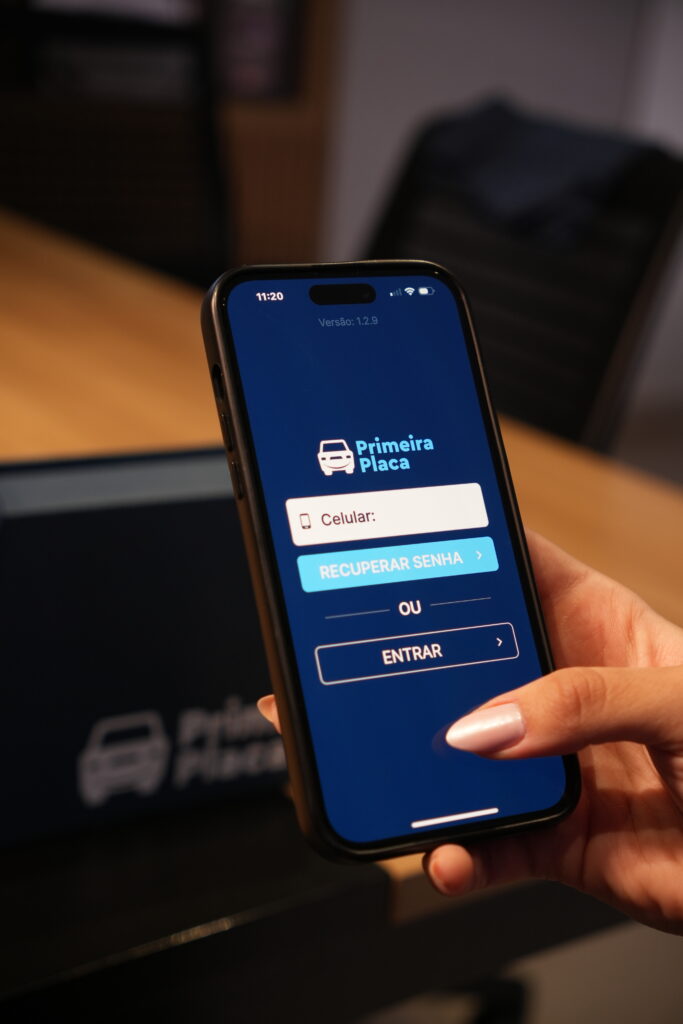Mão de Mulher mostrando Smartphone com aplicativo Primeira Placa em funcionamento, destacando a interface intuitiva.