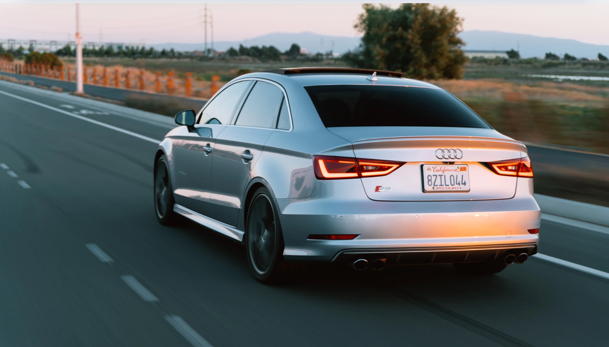 Carro Audi prata em movimento em uma estrada sem placa, simbolizando o motorista que deixar o emplacamento para depois